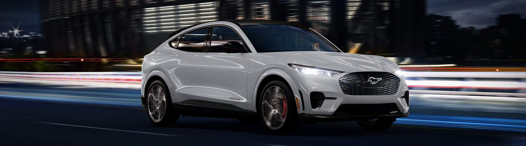 Space White Metallic 2023 Ford Mustang Mach-E® being driven past a stadium at night