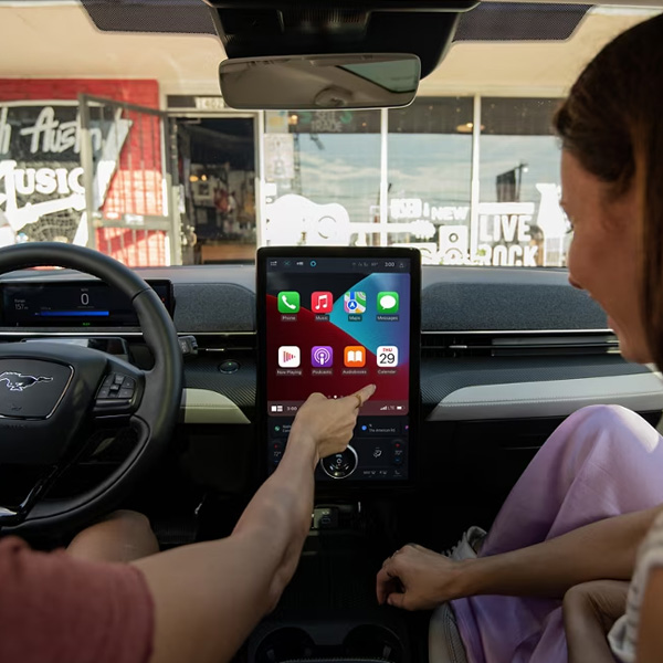 A driver and a passenger are in the front seats of a Ford Mustang Mach-E while using Apple CarPlay