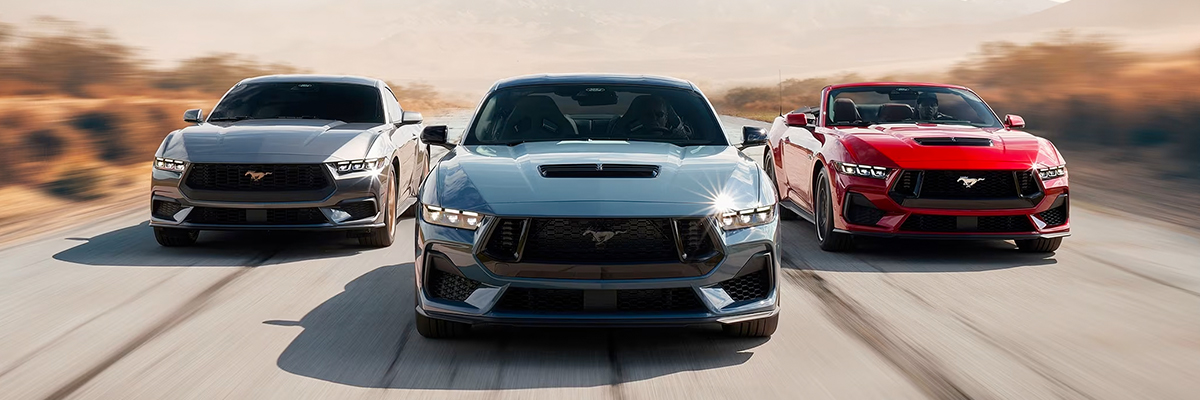Three 2024 Ford Mustang® models, two fastback and one convertible, being driven on a desert road