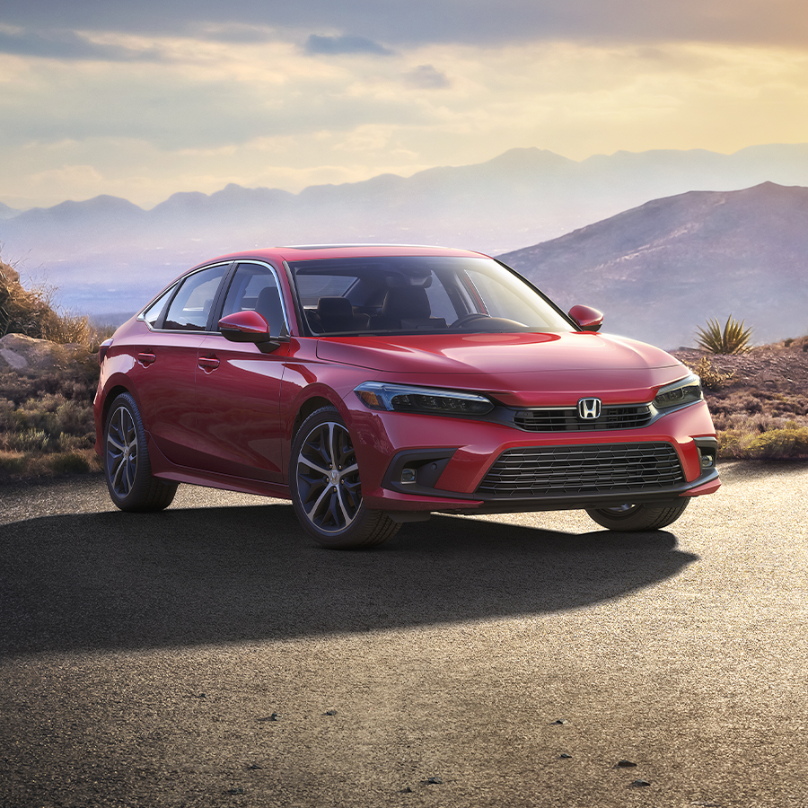 Front passenger-side view of the 2023 Honda Civic Touring Sedan in Rallye Red, parked in a misty parking lot at dusk with mountains in the background.