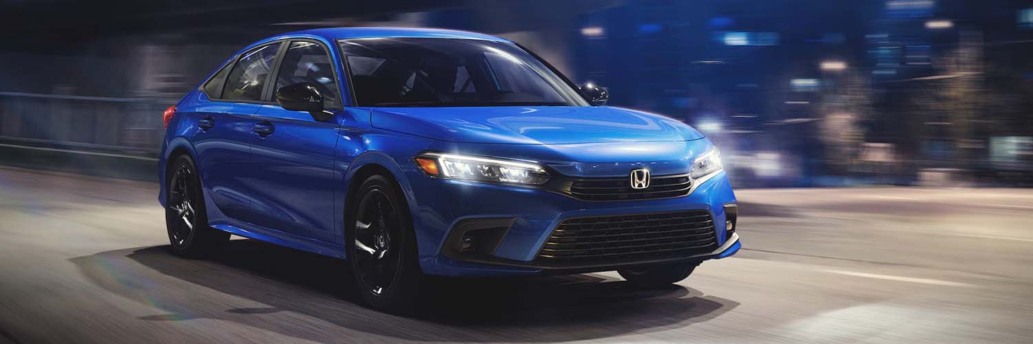 2024 Honda Civic Sport Sedan in Aegean Blue Metallic, driving on a city street at night.