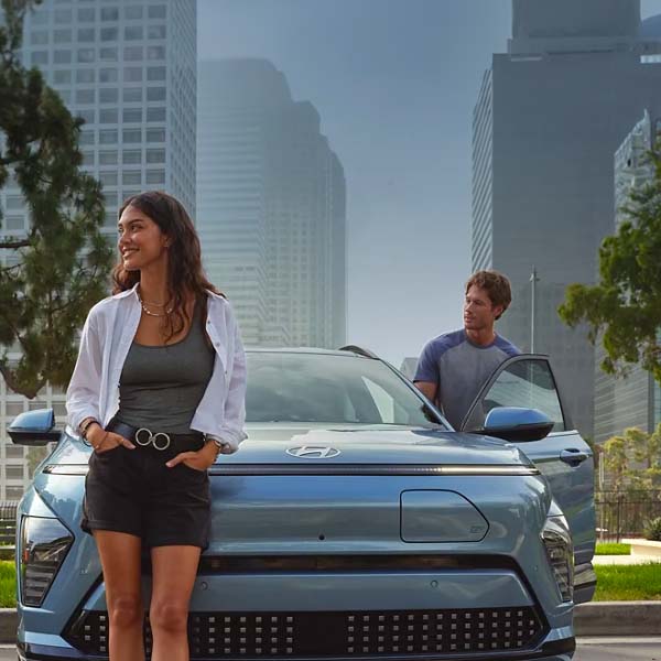 A happy couple leaning against their 2024 Hyundai Kona Electric in a new city