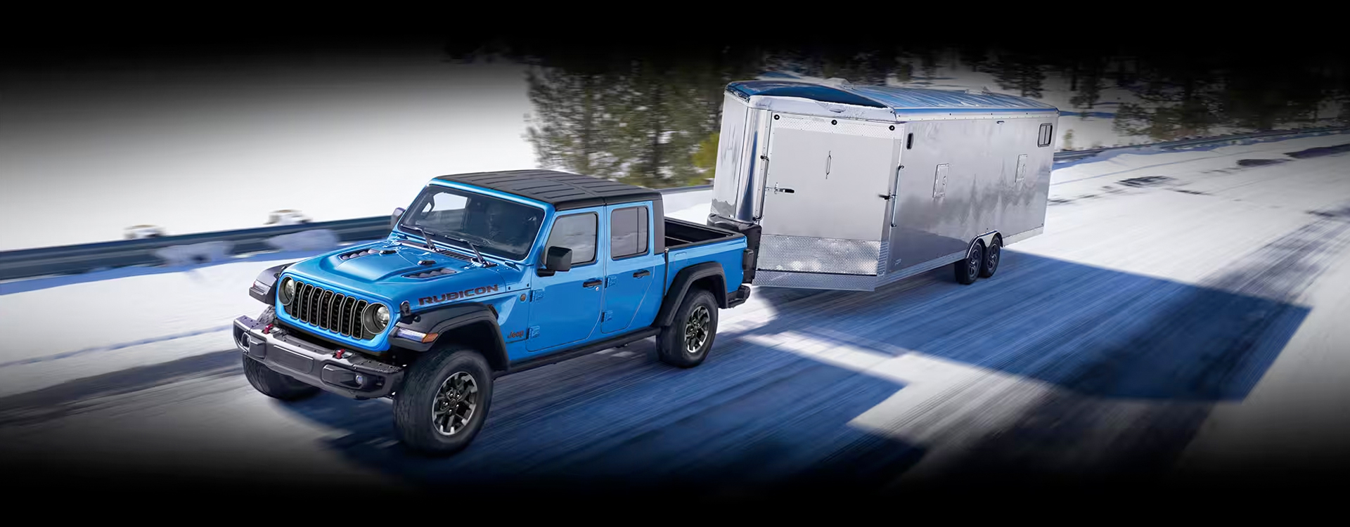 A blue 2024 Jeep Gladiator Rubicon being driven down a snow-covered highway as it tows an enclosed trailer.