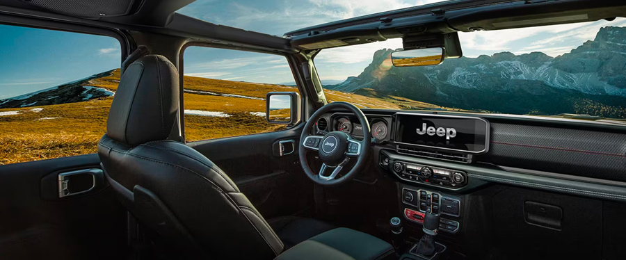 The front row in the 2024 Jeep Wrangler Rubicon focusing on the steering wheel, Uconnect touchscreen, center stack and dash.