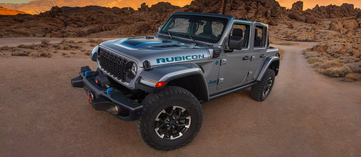 An angled driver-side profile of a gray 2024 Jeep Wrangler Rubicon 4xe parked on a clearing in the desert.