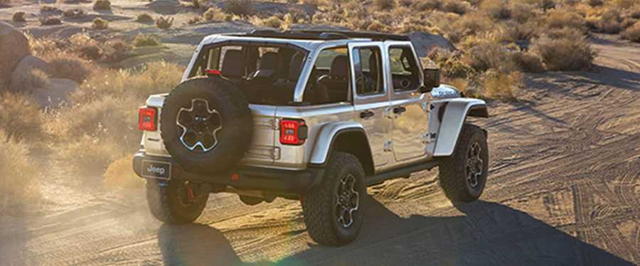 A rear angle of a white 2024 Jeep Wrangler Rubicon 4xe being driven on a sandy trail, off-road in th…