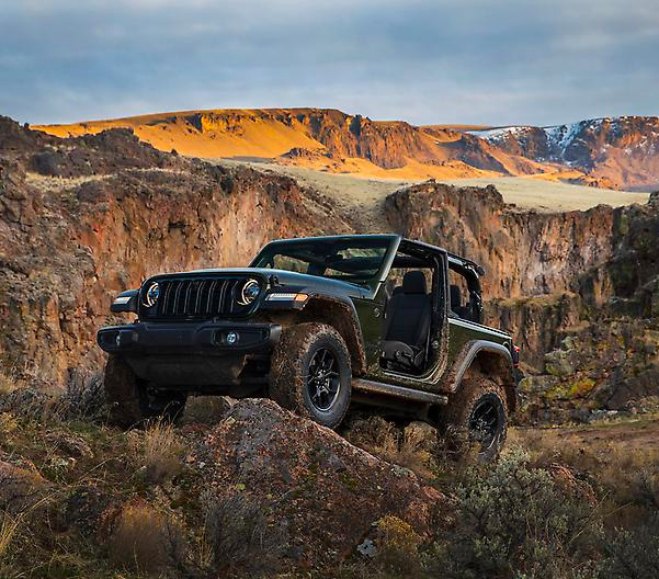 2024 Jeep® Wrangler Willys shown muddy and parked on a rock with canyon background without doors on