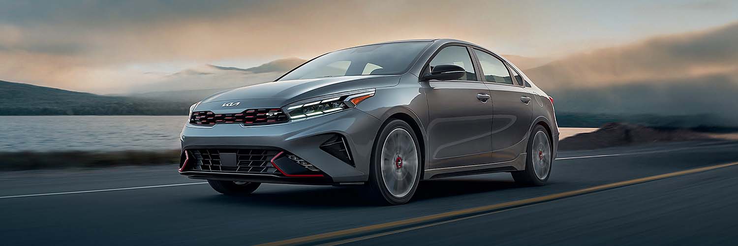 2024 Kia Forte driving on road near ocean showing front three-quarter view