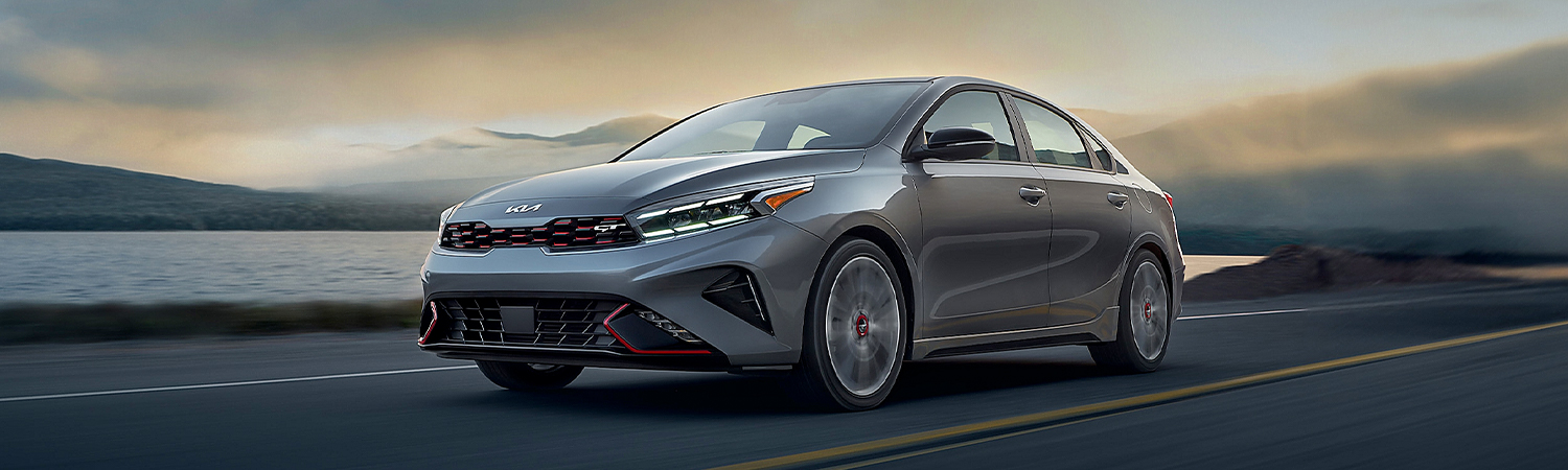 2024 Kia Forte Driving Fast Near A Body Of Water And Mountains Three-Quarter View