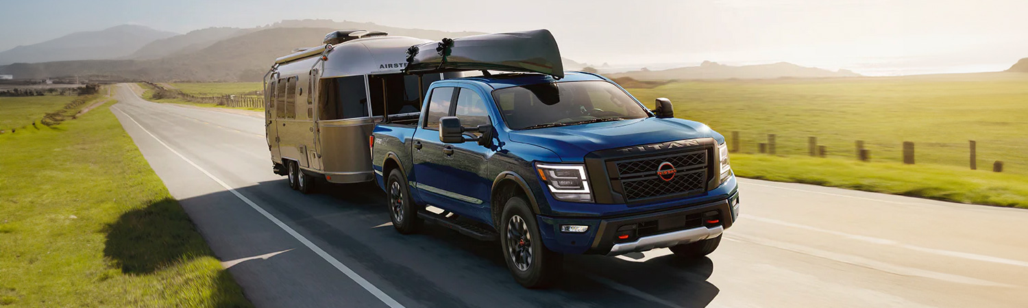 Front 3/4 shot of the 2024 Nissan Titan towing trailer on rural road overlooking farm land