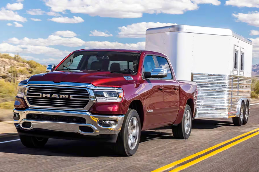 Display A red 2024 Ram 1500 Laramie Crew Cab towing a horse trailer as it is driven down a highway in the desert.