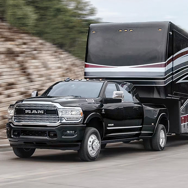 A black 2024 Ram 3500 Limited Crew Cab towing a large fifth wheel travel trailer.