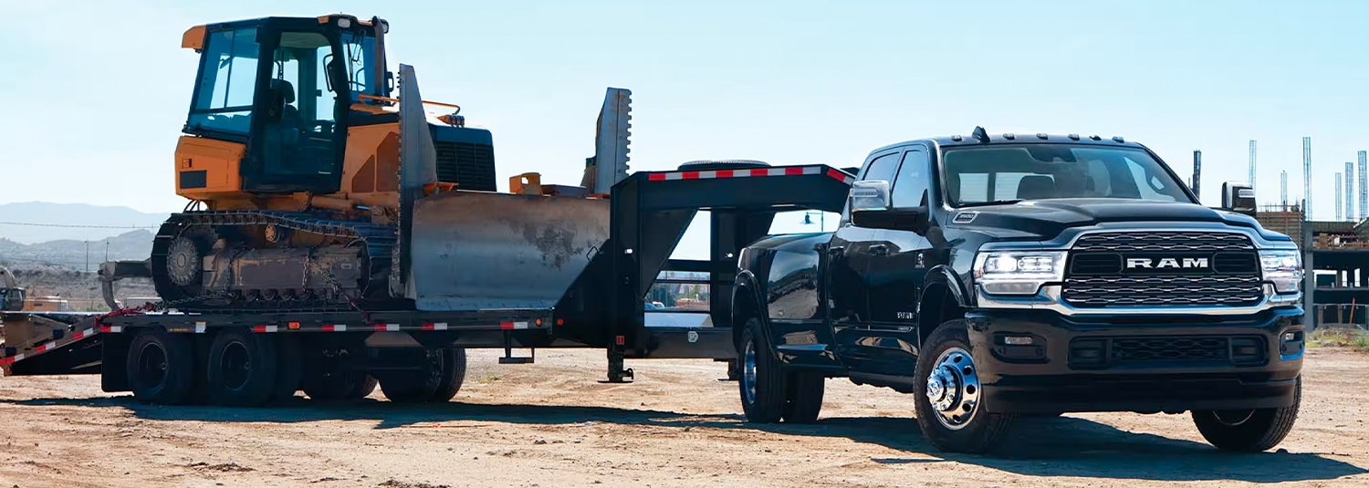 A black 2024 Ram 3500 Limited Crew Cab towing a fifth wheel flatbed trailer with an excavator on it.