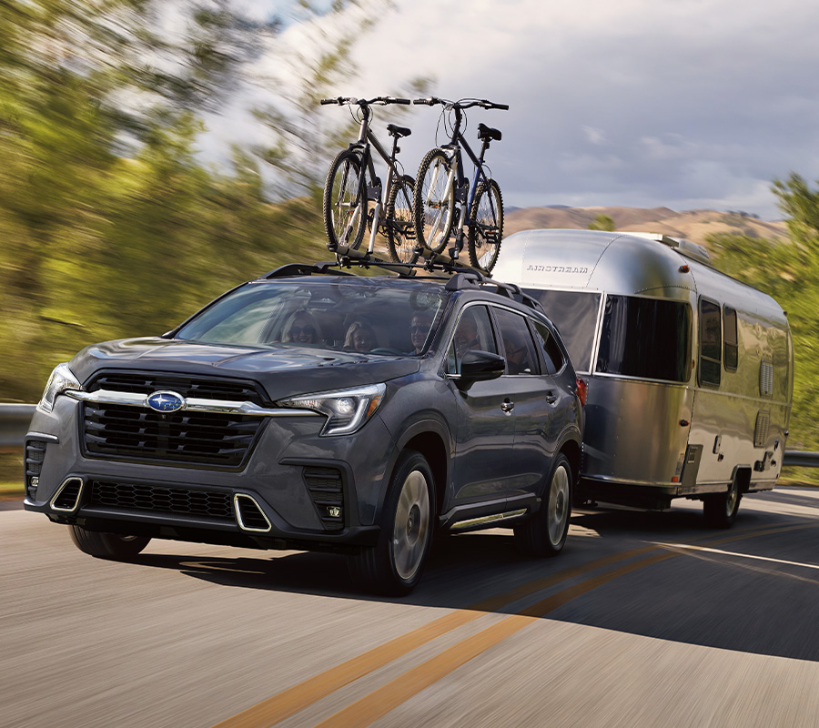 Ascent with Thule Bike Carrier drives uphill towing Airstream trailer, trees and lake in background.