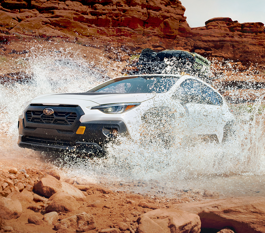 Exterior Action Beauty Major of the 2024 Crosstrek Wilderness driving through a big puddle in the red rocks.