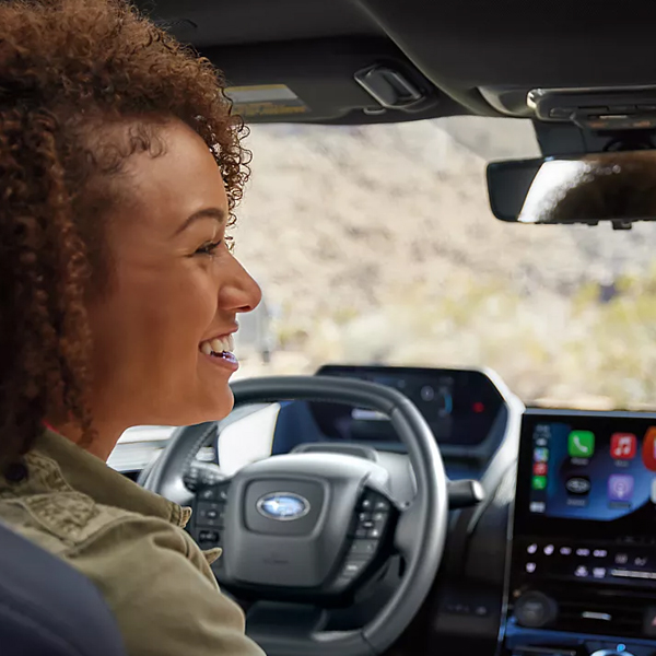 Two women face each other in a Subaru Solterra while one uses Intelligent Assistant voice commands.