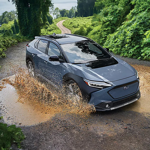 A Subaru Solterra electric family SUV drives through a large puddle on a dirt road.