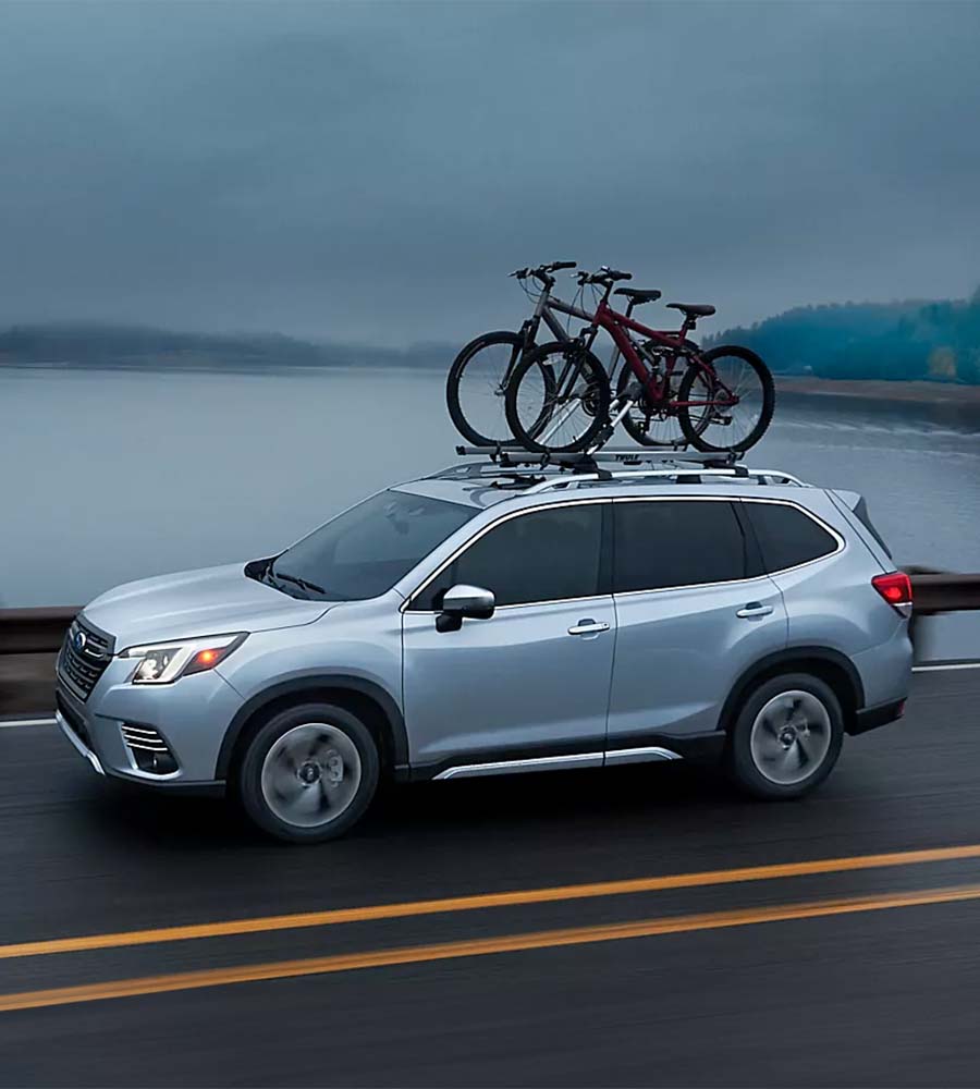 2023 Subaru Forester driving with accessory equipment in front of a lake