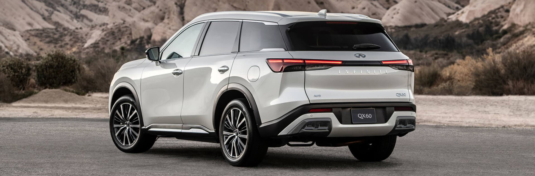 Angled rear view of 2025 INFINITI QX60 Luxury Crossover SUV stopped on road with mountains behind it