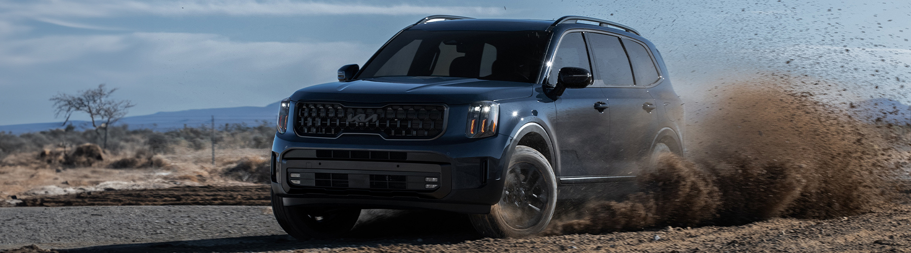 2025 Kia Telluride in a three-quarter front view, making a strong turn that causes dirt to fly in the air