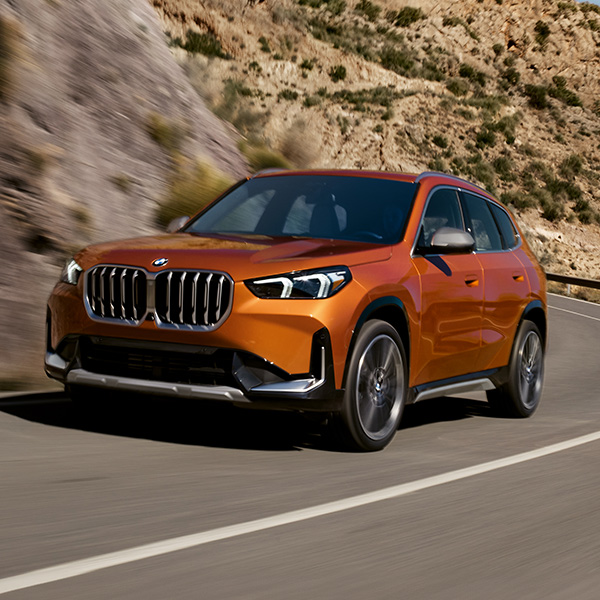 Front 3/4 shot of the 2025 BMW X1 driving up winding road