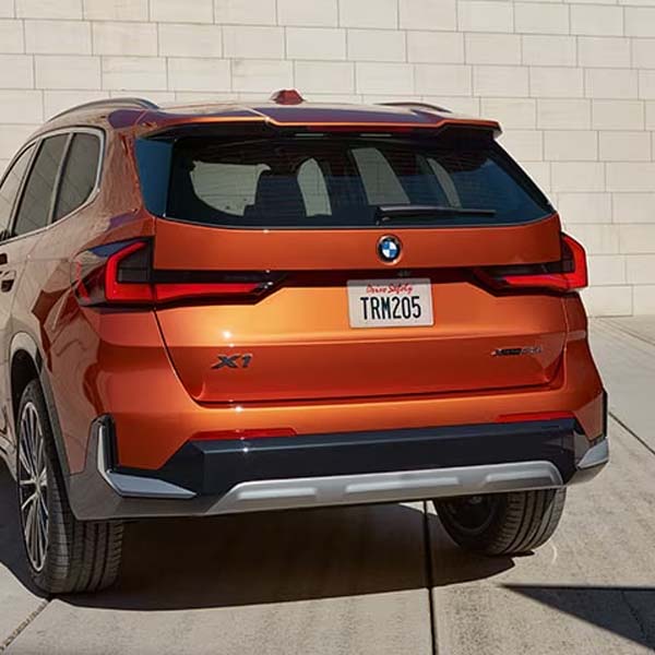 Rear of orange 2025 BMW X1 parked in front of brick wall