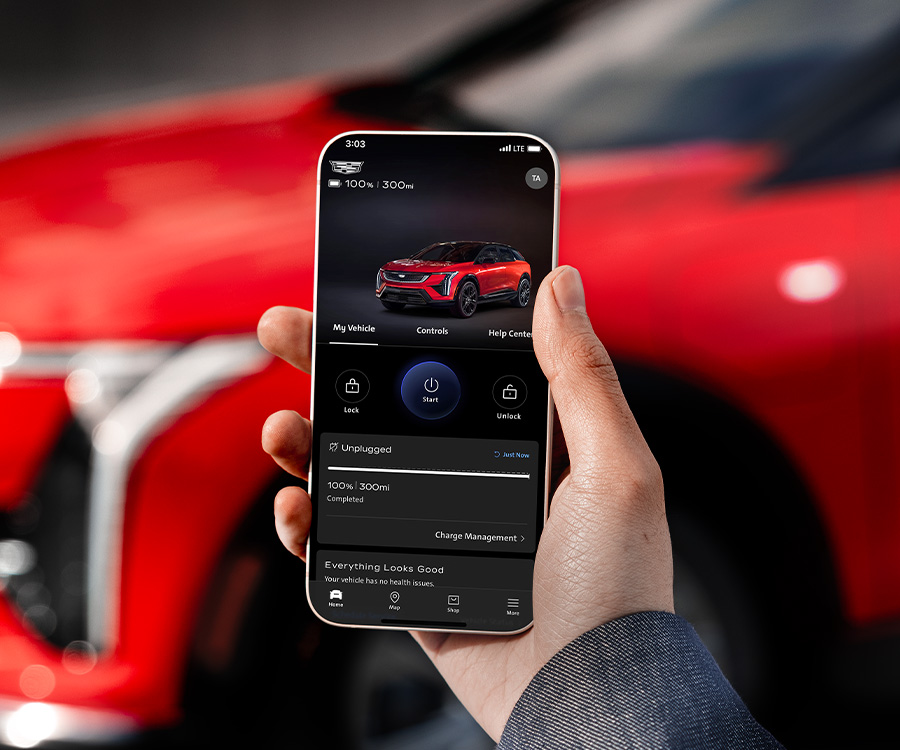 2025 Cadillac Optiq, Sport 2 (6MR26), exterior detail, red, Monarch Orange (GAG), 21 Inch wheel (RVU), parked, driver side, with male talent, wearing glasses, over shoulder, holding cell phone, mobile, app, vehicle in background, status information