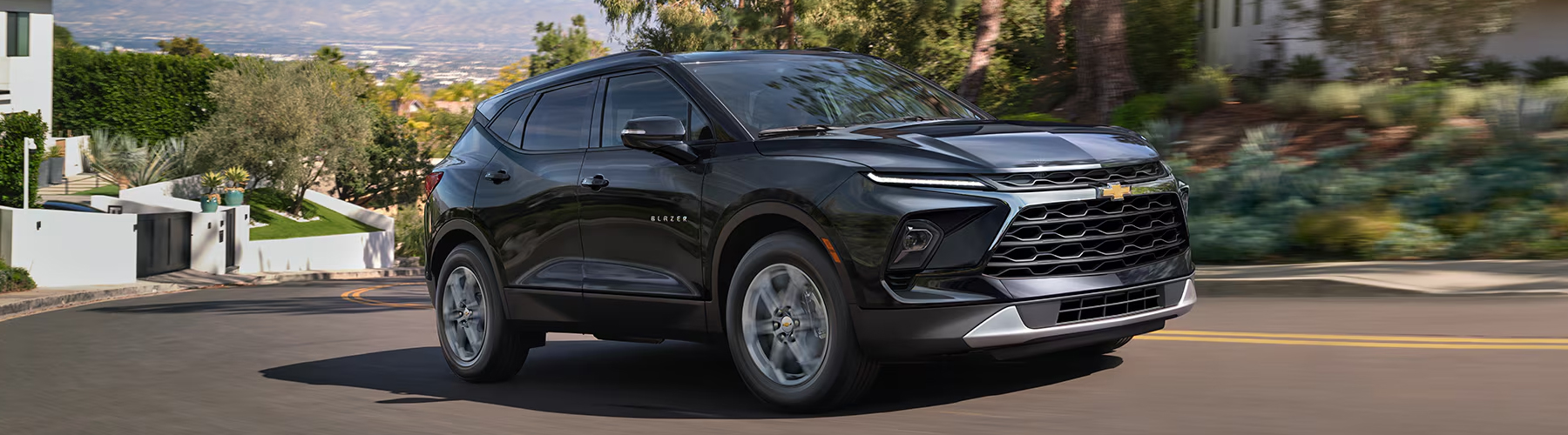 A Black 2025 Chevy Blazer driving Next to a Building on a Sunny Day