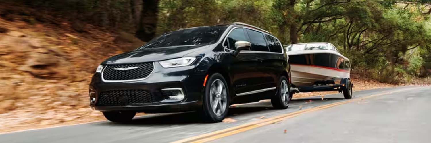 A black Chrysler Pacifica racing down a rural road towing a boat.
