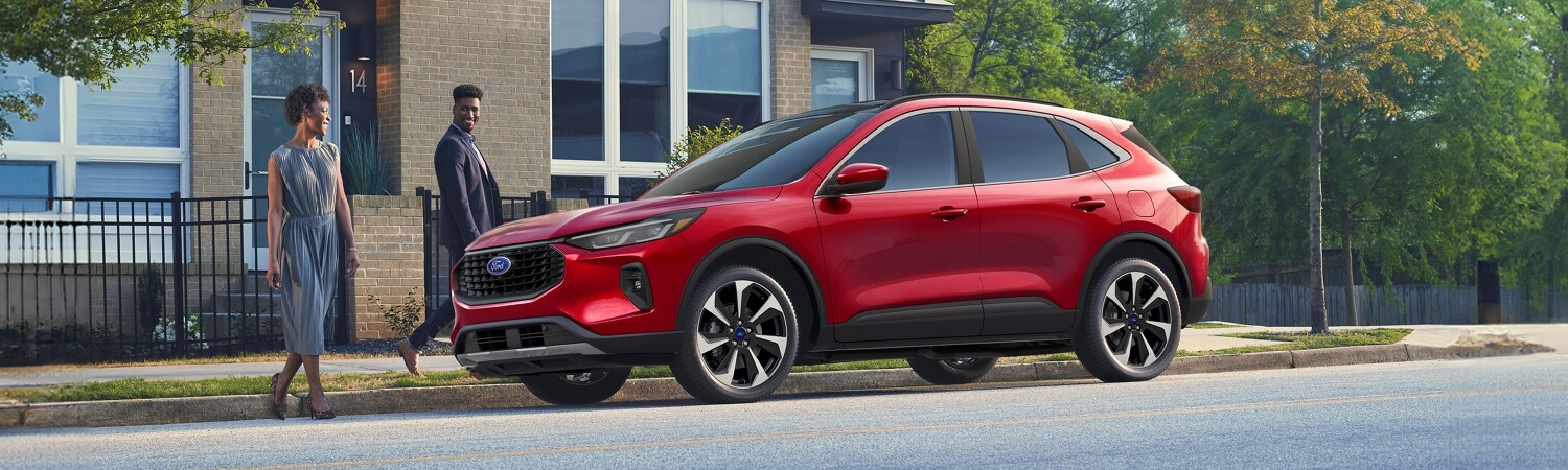 Two people walking toward a parked 2025 Ford Escape® SUV in Rapid Red Metallic Tinted Clearcoat (extra-cost paint)