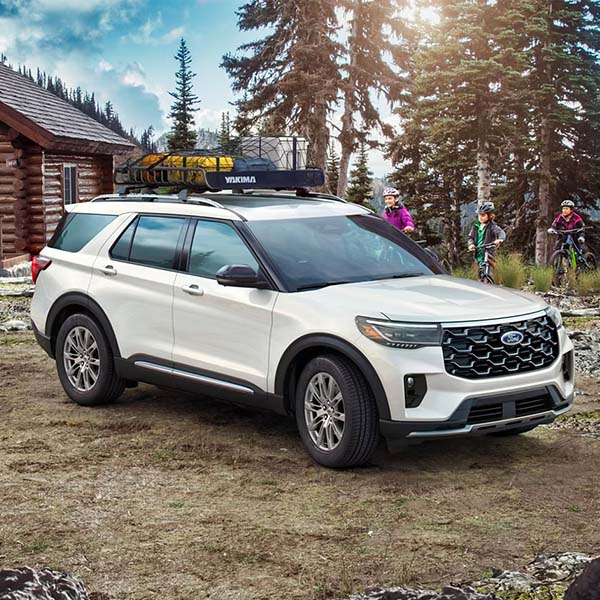 2025 Ford Explorer with camping gear packed in the roof racks in front of a cabin