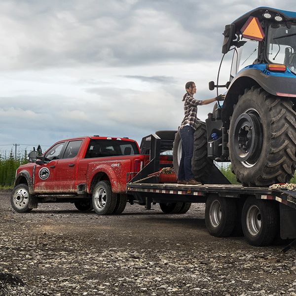 2025 Ford Super Duty® F-450® XL in Race Red pulling a trailer carrying a large tractor