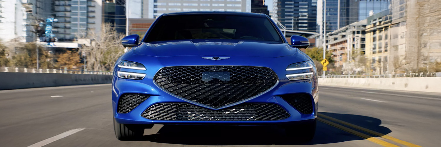 Blue 2025 Genesis G70 driving down city street.