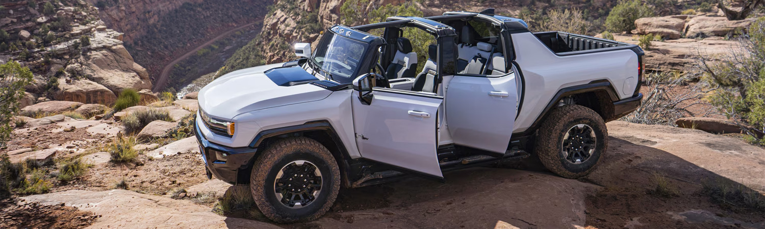 White 2025 GMC HUMMER EV Pickup parked in mountains with doors open.