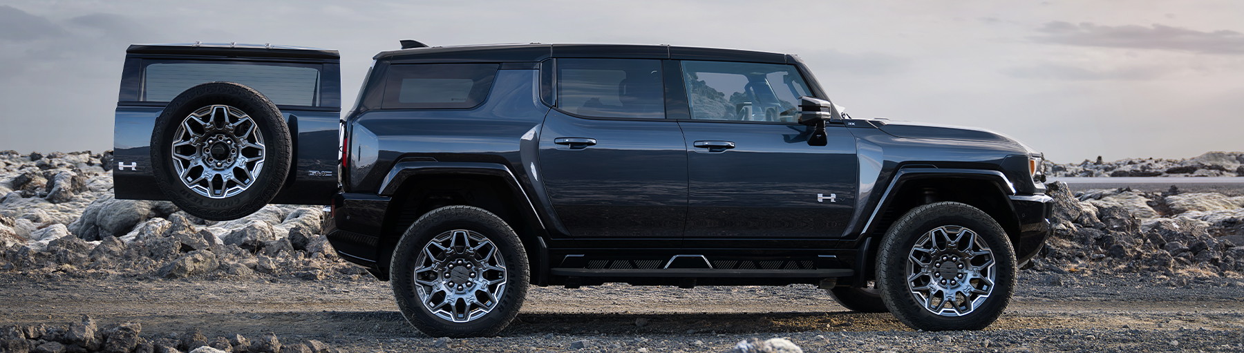 Side View of a Black GMC Hummer EV SUV On a Rocky Plain with the Trunk Door Opened