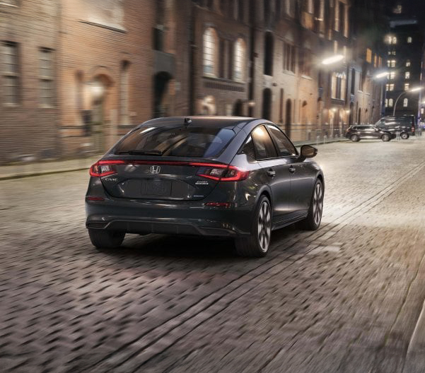 Rear view of a black 2025 Honda Civic Hatchback driving down a road