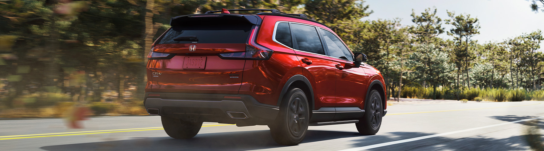 Rear 2024 CR-V Sport Touring Hybrid Rear passenger-side view of the 2025 Honda CR-V on a two-lane highway.