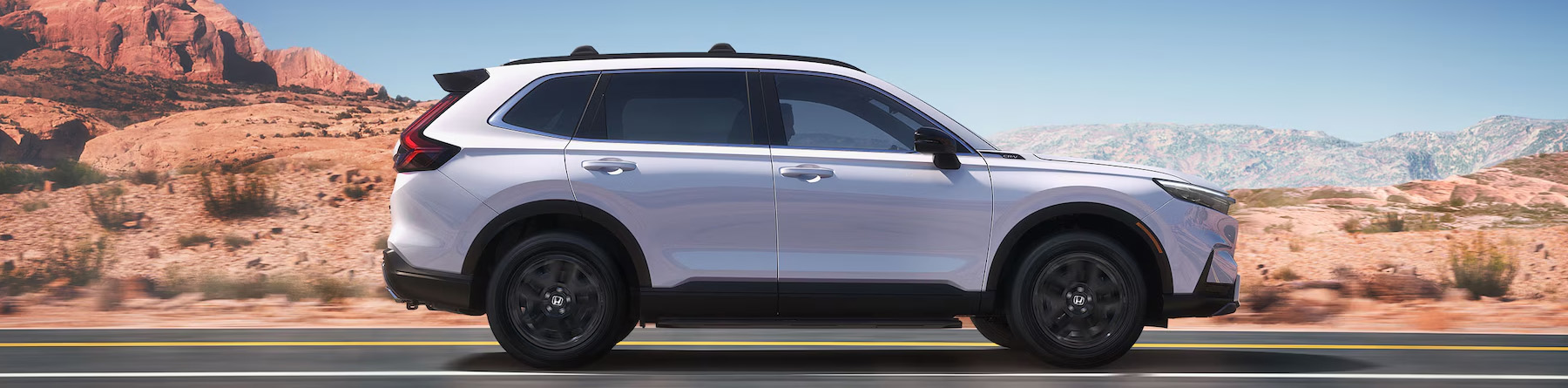 Passenger-side profile view of the 2025 Honda CR-V Sport Touring Hybrid driving through the desert.