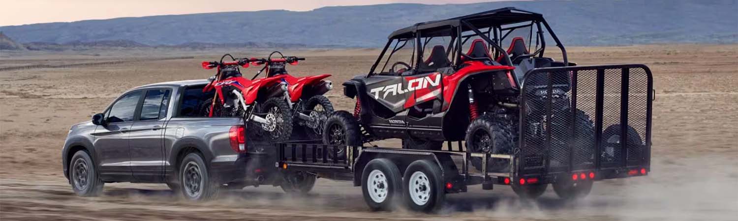 2025 Honda Ridgeline towing ATVs and UTV on desert road.