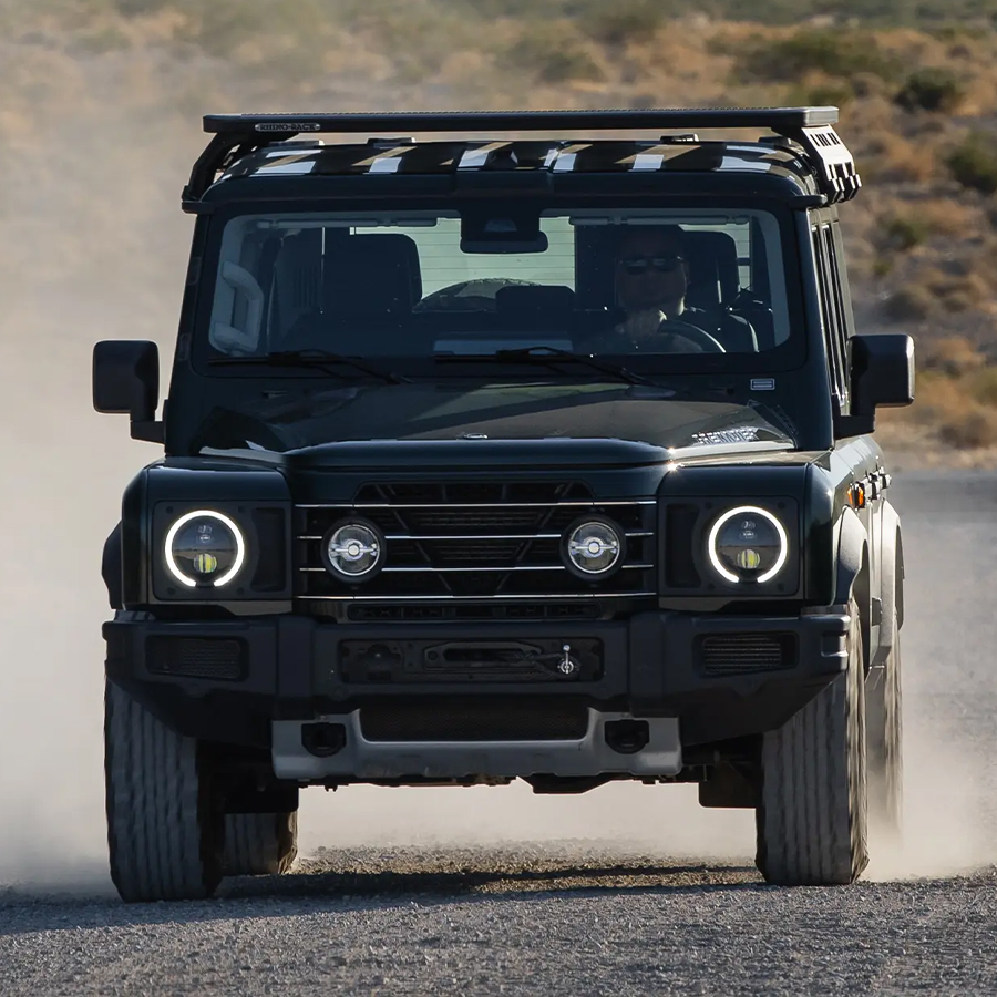 Front view of an INEOS Grenadier kicking up dust while driving on a desert track.