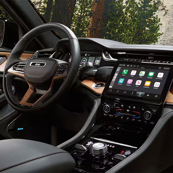 The interior of a 2025 Jeep Grand Cherokee Summit Reserve focusing on the steering wheel, Uconnect touchscreen, center stack and front passenger touchscreen.