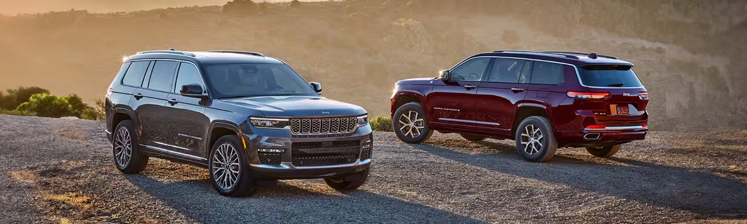 Display A gray 2025 Jeep Grand Cherokee Summit Reserve and a red Jeep Grand Cherokee Limited parked opposite of each other on a gravel mountain road at sunset.