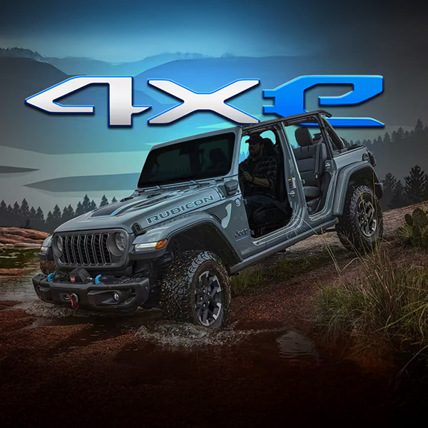 A silver 2025 Jeep Wrangler 4xe Rubicon 4xe with its doors removed, descending a hill as it enters a stream. Mountains are drawn in the background. 4xe.