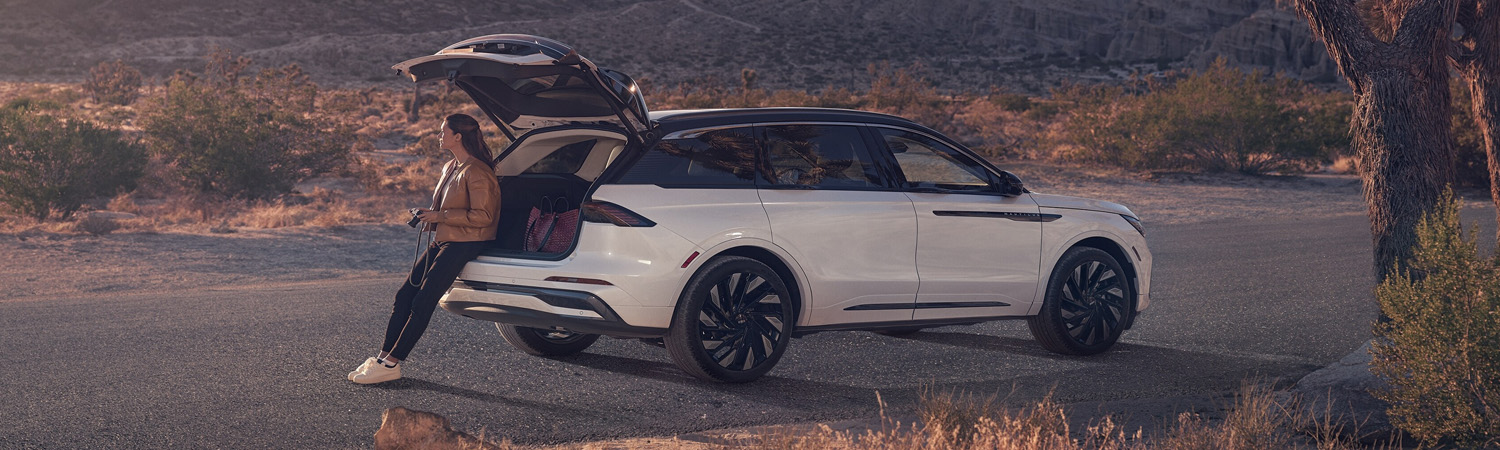A person is shown sitting on the rear bumper of a 2025 Lincoln Black Label Nautilus® SUV with the rear liftgate open