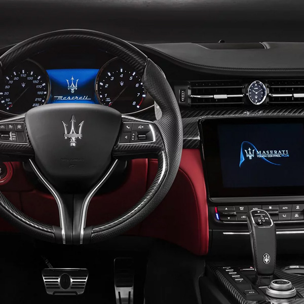 Close-up interior view of the 2025 Maserati Grecale, featuring a sporty black steering wheel with red trim, digital cluster, and dual central touchscreens.