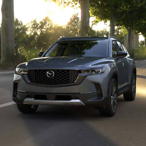 2025 MAZDA CX-50 driving on a road with trees in the background.