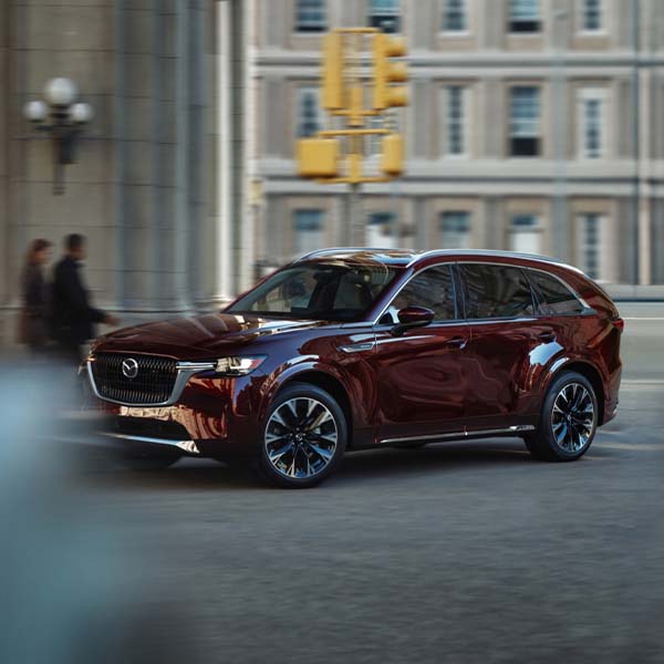 A maroon 2025 MAZDA CX-90 PHEV parked in a city street.