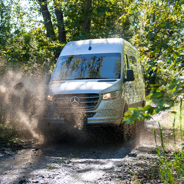 Head on shot of the 2025 Mercedes-Benz Sprinter Crew driving through muddy terrain