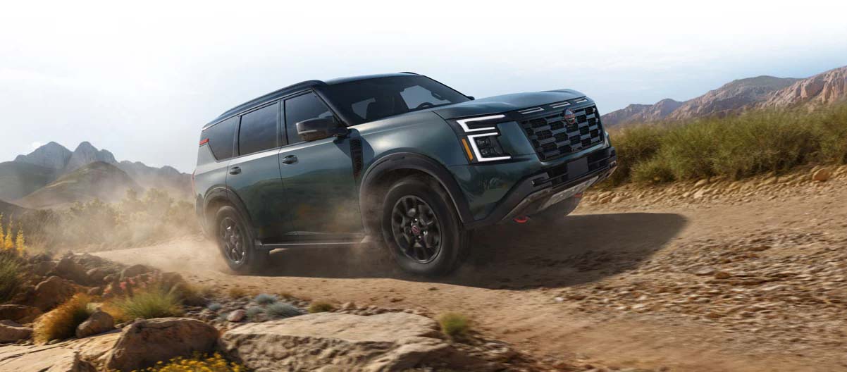 A green 2025 Nissan Armada driving along a rural dirt path