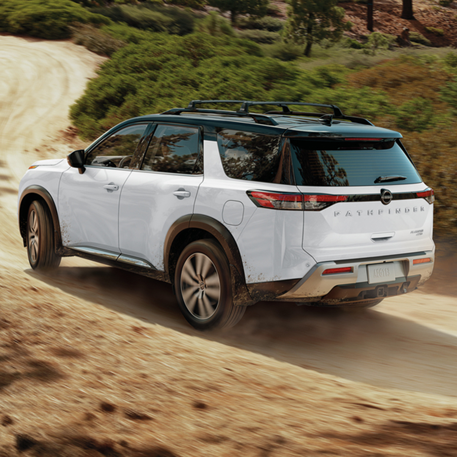 2025 Nissan Pathfinder rear 3/4 view driving down a dirt mountain road.